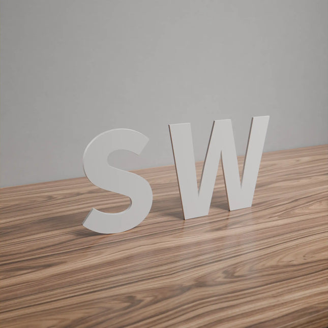 Flat cut acrylic letters SW in white, displayed on a wooden surface against a plain wall